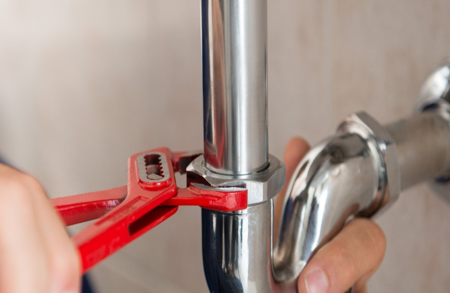 A plumber using a small, red wrench to tighten the connection on a P-trap underneath a sink during an appointment for drain repair in the Hamptons, NY.