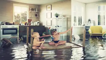 Two kids use an upside down kitchen table as a raft in their flooded kitchen.
