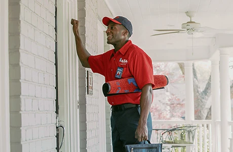 Amiling African American male Mr. Rooter tech knocking on door of residential home.