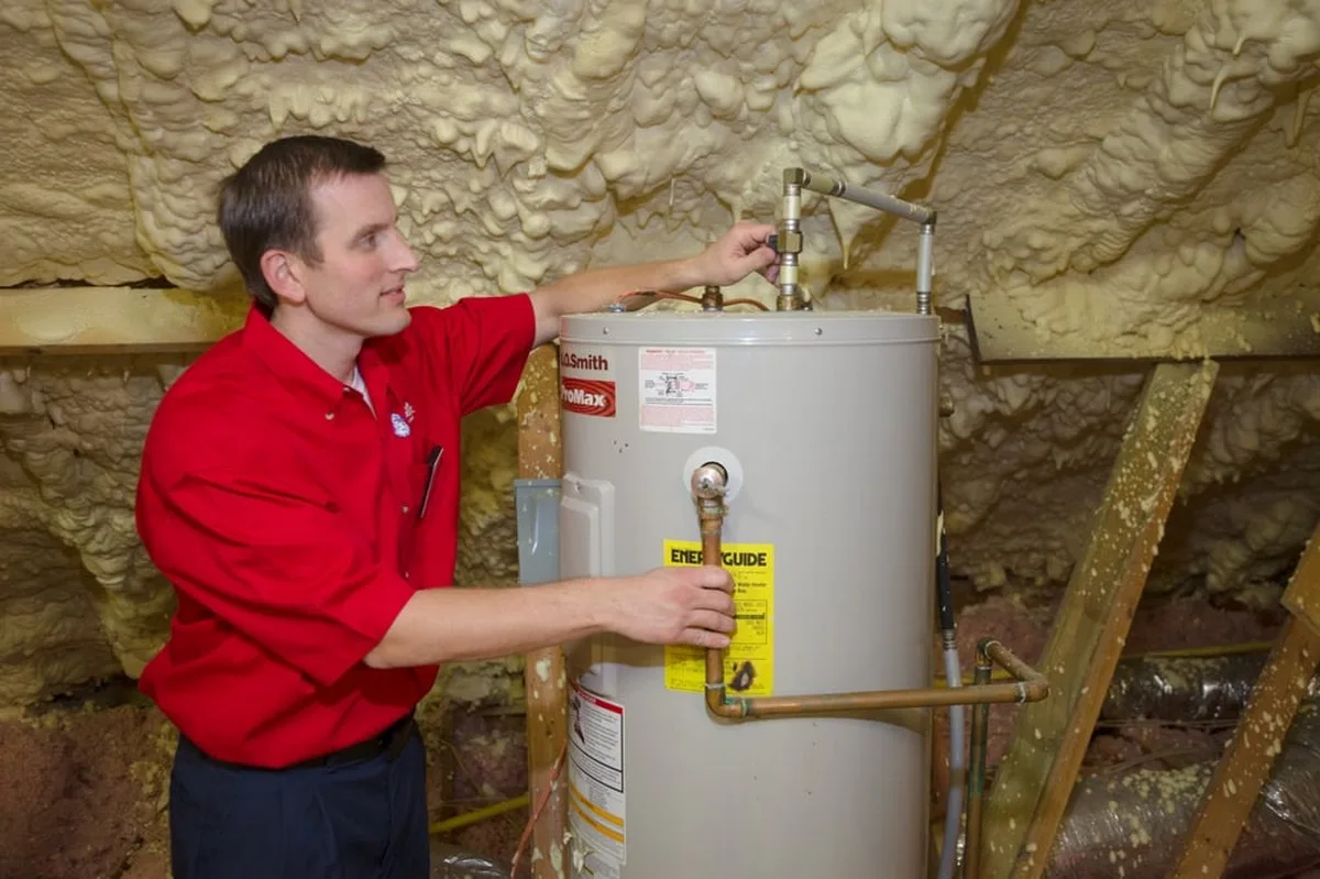 Mr. Rooter plumber installing a water heater in an unfinished space with exposed insulation.