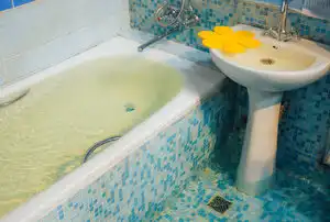 Tub and sink overflowing with water in blue-tiled bathroom.