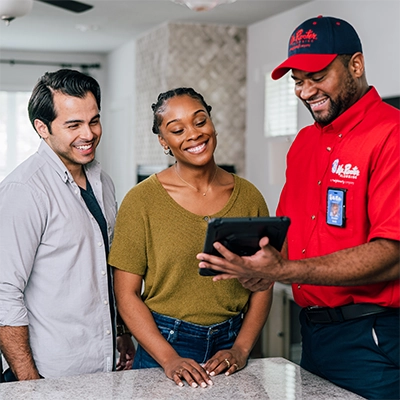 Mr. Rooter Plumbing professional showing two customers something on a tablet.