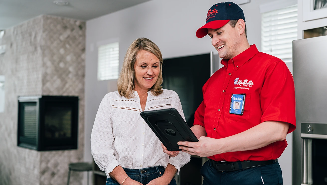 Mr. Rooter technician showing a customer pipe lining service options on a tablet.