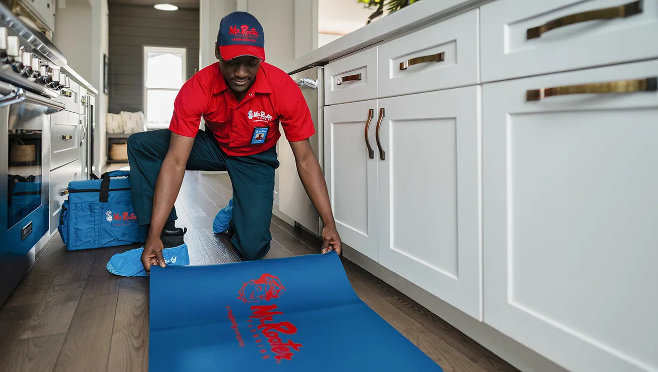 Mr. Rooter technician laying out a rug in front of the sink.