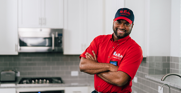 Smiling Mr. Rooter technician standing in a kitchen with his arms crossed.