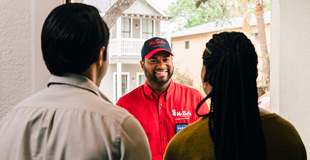 Two customers greeting a Mr. Rooter technician at the front door of their home.