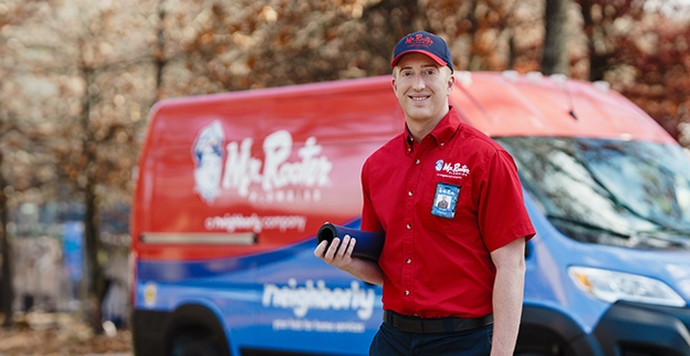 Mr. Rooter professional standing beside a red branded van.