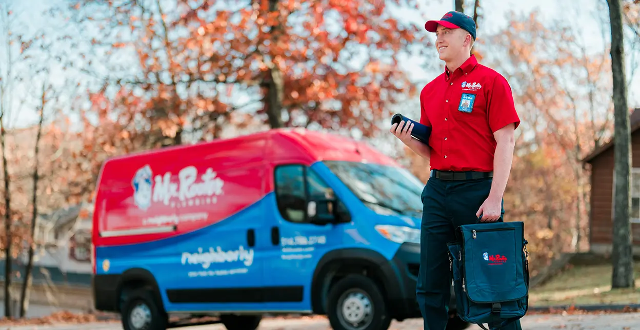 Mr. Rooter professional walking up to a customer's home with a branded van parked in the background.