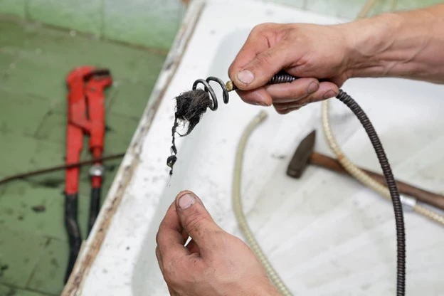 alt="A Mr. Rooter plumber removing hair from a clogged shower with a plumber’s snake.