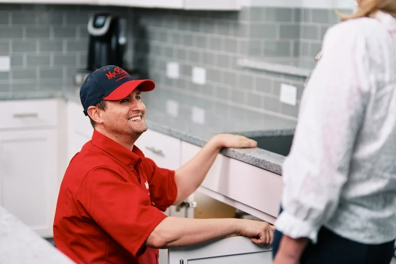 Mr. Rooter plumber explaining drain repair to customer in a kitchen.