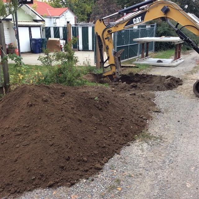 Digger beside large pile of dirt outside residential home.