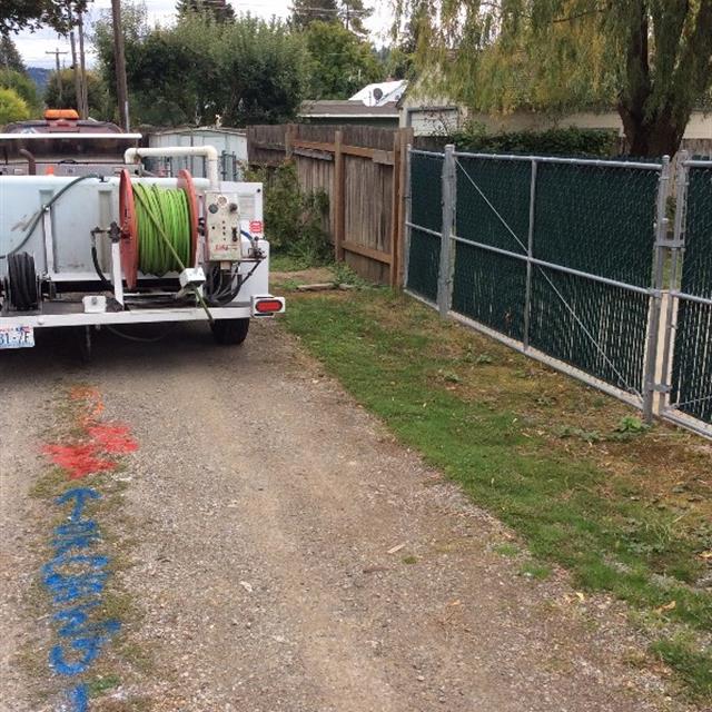 Work truck parked on dirt road marked with red and blue spray paint indicating location of plumbing.