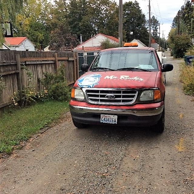 Red Mr. Rooter branded van parked on dirt road.