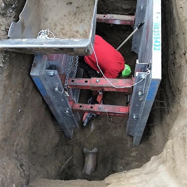 Mr. Rooter plumber inside steel structure in hole created by digger.