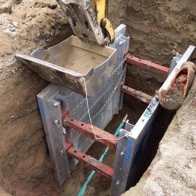 Digger placing steel structure into dirt hole.