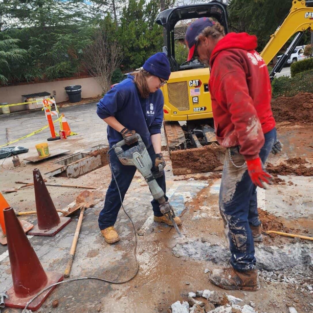 Two Mr. Rooter employees using a jack hammer and other equipment.