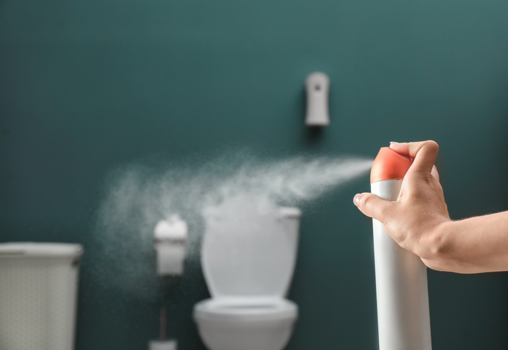 Woman spraying air freshener in bathroom.