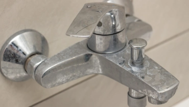 Close-up of shower mixer faucet with limescale, white chalky deposit and stains.
