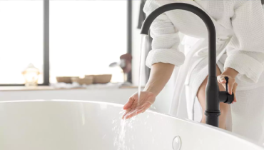 A person testing the water coming out of a bathtub faucet.