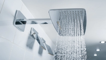 Water coming from a square shower head in modern bathroom with white tile