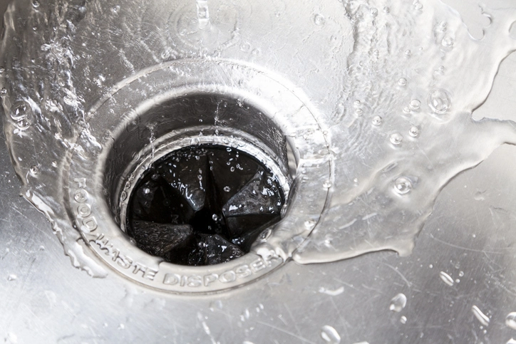 A close-up of a garbage disposal in a stainless steel kitchen sink with water flowing into it. | Mr. Rooter® Plumbing of Southeast Georgia