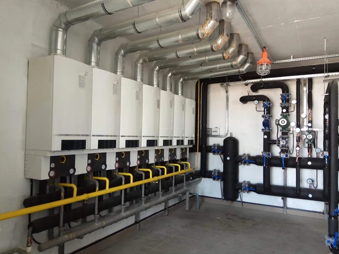 A large commercial boiler room with multiple water heaters and an intricate network of pipes and gauges.