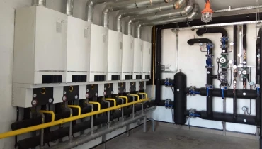 A large commercial boiler room with multiple water heaters and an intricate network of pipes and gauges.