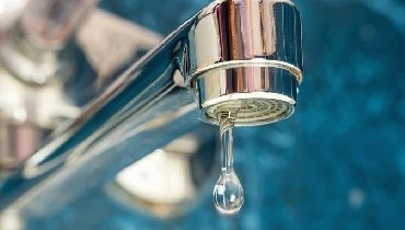 A close-up of a stainless steel faucet with a single drop of water coming out of it, indicating low water pressure. | Mr. Rooter Plumbing of Yavapai, Coconino and Maricopa Counties