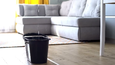 A bucket catches a stream of water leaking from the ceiling.
