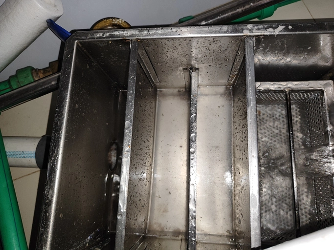 Top view of a dirty grease trap with water flowing.