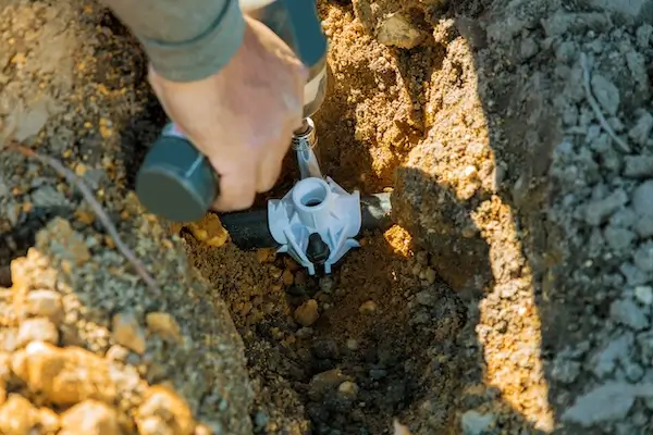 A plumber performing commercial irrigation system installation in a trench.