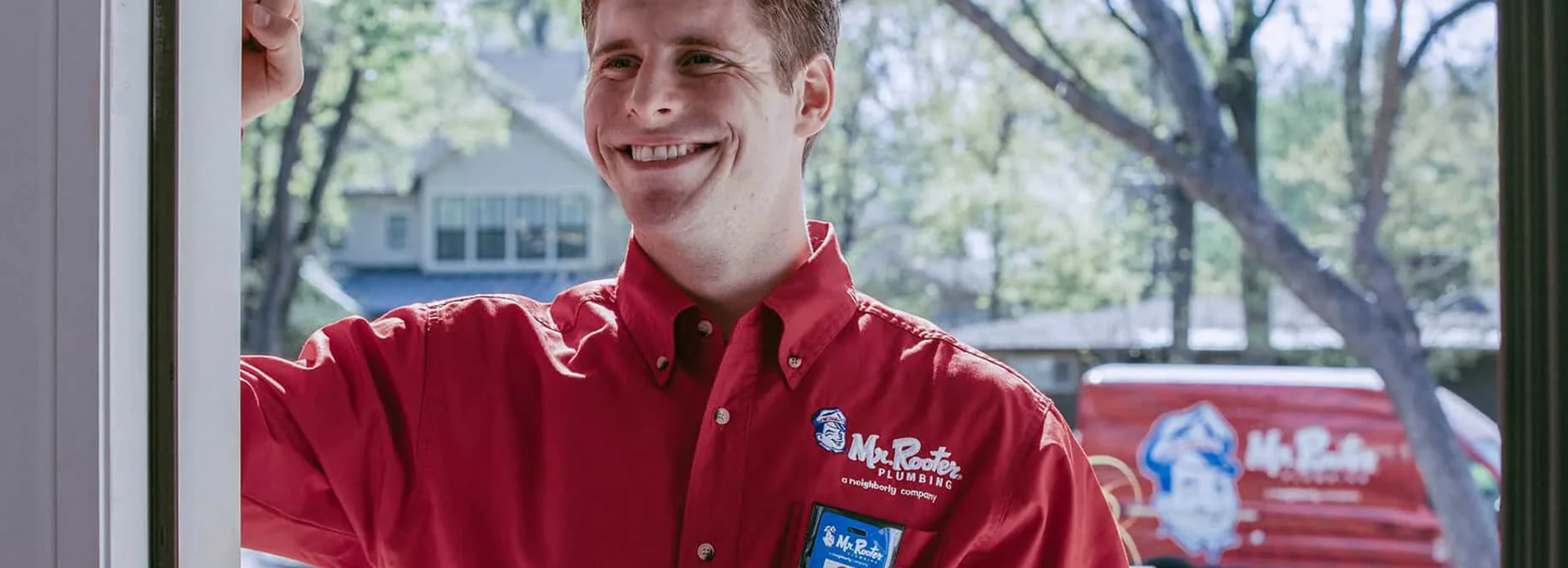 Smiling male Mr. Rooter employee in red branded button down shirt at door of customer's home.