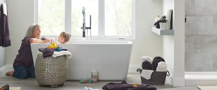 A lady laughing with a young child that is in the bathtub.