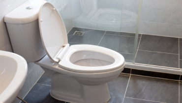 A white porcelain toilet on a dark tile floor. | Mr. Rooter Plumbing of Southeast Georgia