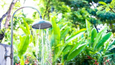 Outdoor shower sprinkling water with foliage in background.