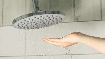 Female hand touching water pouring from a rain shower head, checking water temperature.