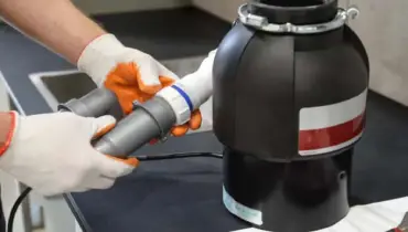 A close-up image of someone holding a sink’s p-trap next to a garbage disposal sitting on the counter after it has been removed in order to complete garbage disposal repairs.