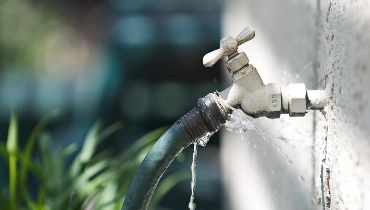 A hose bib with a garden hose connected to it and water spraying out around the point where the hose connects.