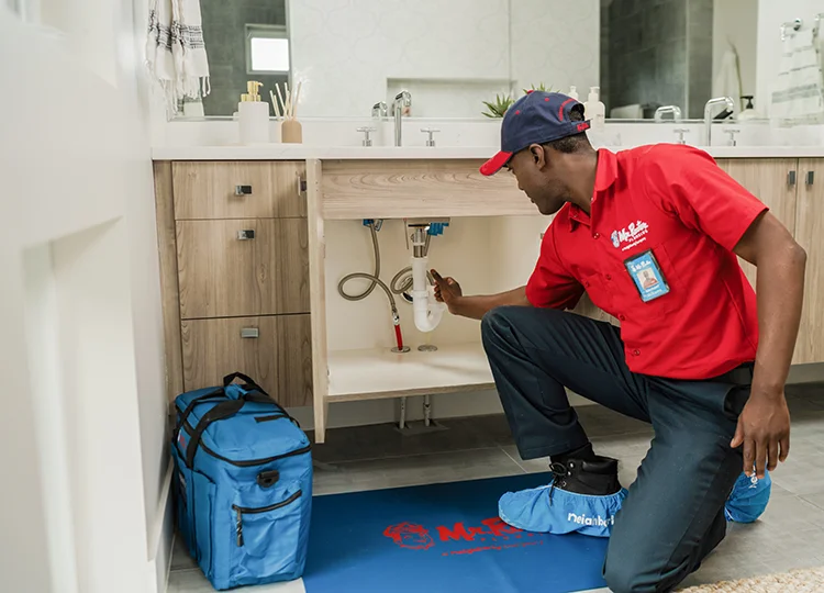 Mr. Rooter plumber doing pipe leak repair work under a bathroom sink.