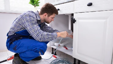 Young Male Plumber Cleaning Clogged Sink Pipe In Kitchen.