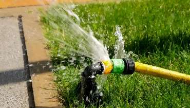 Closeup of water leaking and flowing on green grass lawn through a damaged hose pipe.