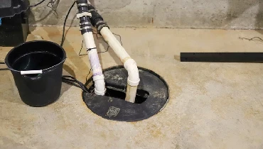 Two PVC pipes are seen coming from a sump pit in a concrete floor.