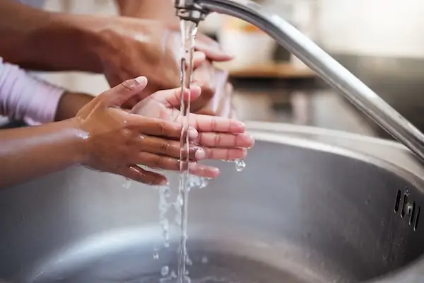 Young girl and man washing their hands with clean water from water well pump