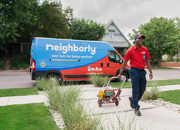 Mr. Rooter Plumbing walking up to a home with drain service equipment