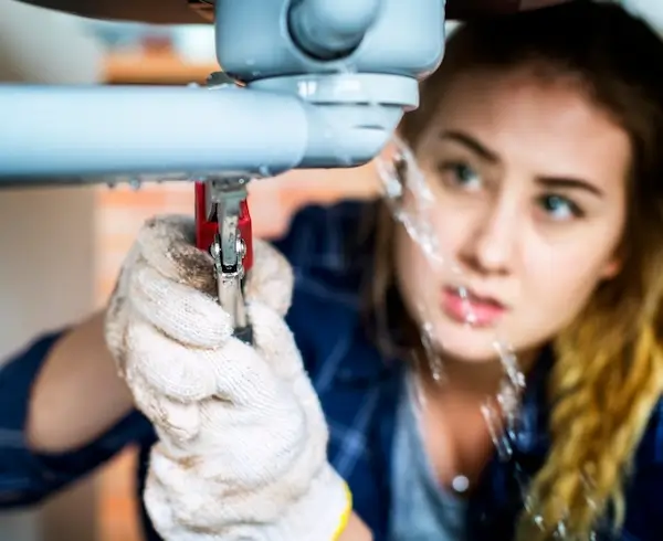 Woman handling plumbing emergency repair on leaking pipe 